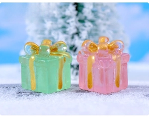 Detailed macro view of miniature luminous resin gift boxes with gold bows on snowy background
