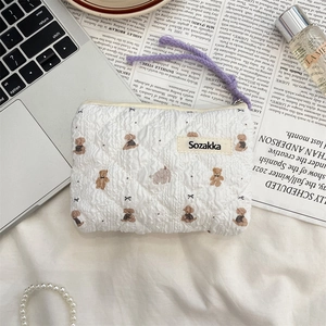 Detail of quilted white bag with brown teddy bear pattern and purple braided zipper pull