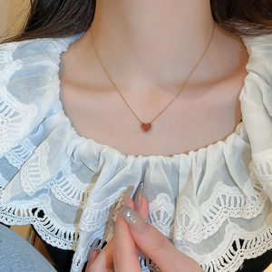 Gros plan d'un collier doré avec un délicat pendentif coeur rouge porté par un mannequin