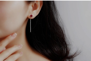 Detail of elegant silver ear threaders with red zircon tassel worn by model