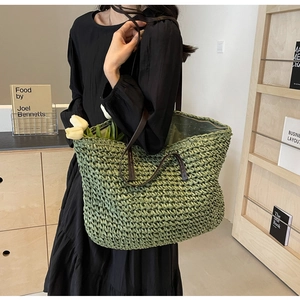Close-up of green woven straw tote bag with brown leather shoulder straps and tulip detail