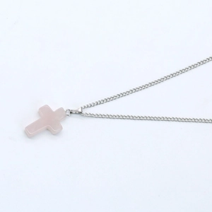 Macro shot of silver chain with translucent pink crystal cross pendant on white background