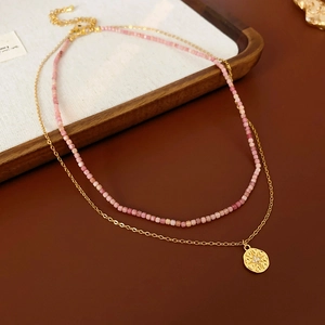 Détail d'un collier de perles à double rangée avec pendentif pièce en or sur bois