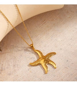 Close-up of golden starfish pendant with textured finish on a minimalist beach theme base