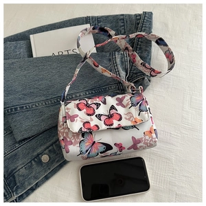 Detailed view of white butterfly print flap crossbody bag on denim jacket backdrop