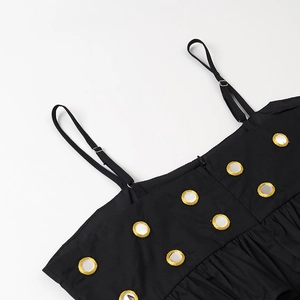 Détail d'une robe à bretelles noire avec ornement d'anneau doré et tissu plissé