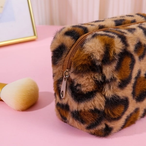 Close-up of leopard print plush cosmetic bag with metal zipper on a pink surface