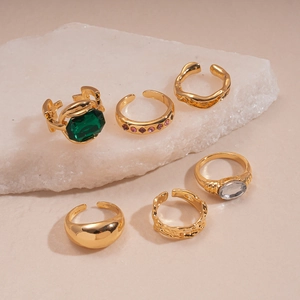 Set of 6 gold vintage rings with green emerald, clear gem, and pink zircon on white stone