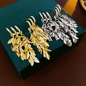 Detailed view of gold and silver leaf tassel earrings on a dark green jewelry box