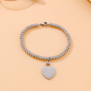 Detail of silver beaded chain bracelet featuring a polished heart charm and lobster clasp
