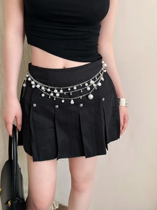 Detail of layered waist chain with pearls and star charms on a black pleated skirt