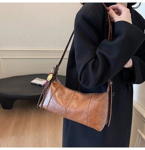 Close-up of a brown leather shoulder bag with vertical stitching and a yellow smiley charm