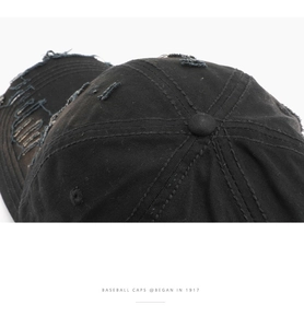 Detailed close-up of distressed ripped texture and stitching on a black baseball cap