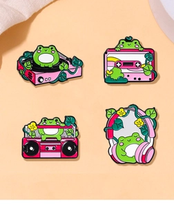 Detailed view of four pink enamel pins featuring cartoon frogs on vintage music devices