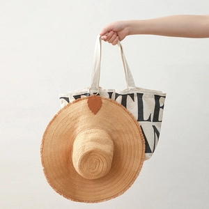 Leaf-shaped brown PU leather magnetic hat clip holding a straw hat on a canvas bag handle