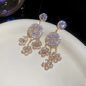 Close-up of golden floral tassel earrings with white cubic zirconia on ceramic plate
