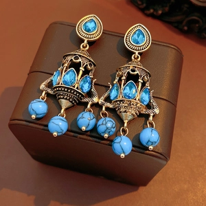 Close-up of vintage gold chandelier earrings with blue crystals on a leather jewelry box
