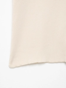 Detail of light beige knit fabric showing fine stitching and smooth hem texture