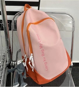 Detail of a large pink and orange patchwork backpack on a transparent chair with a plush charm