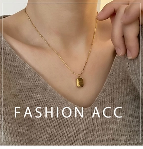 Detail showing a golden square pendant necklace on a model with a soft knit sweater