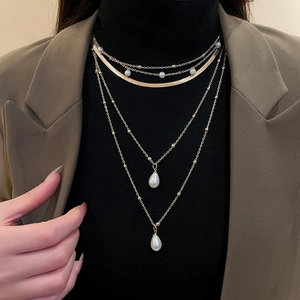 Detail of layered gold necklace with teardrop pearls on a brown suit and black turtleneck
