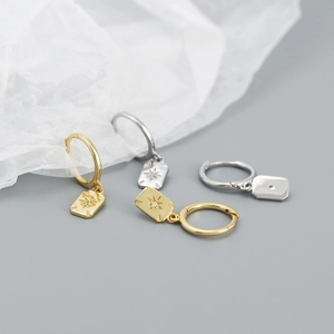 Detailed view of silver and gold starburst square pendant earrings on grey background