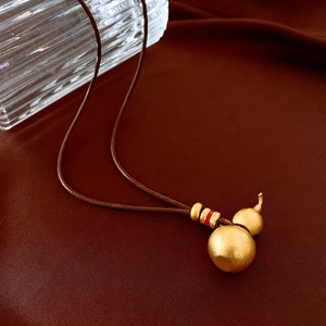 Detail of matte gold gourd pendant with brown cord on elegant dark red silk background