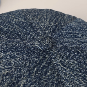 Macro detail of dark blue denim baker boy hat top with textured fabric and central button