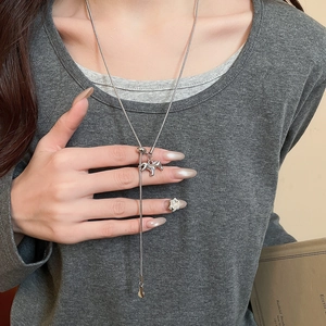 Detail view of a long silver horse pendant necklace worn on a grey textured shirt