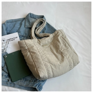 Flat lay of large beige quilted nylon tote bag with denim jacket and magazine