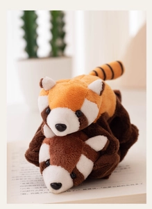 Detail of red panda plush toys with striped tails resting on an open book