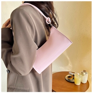 Pink minimalist baguette bag with knotted shoulder strap shown in a lifestyle setting