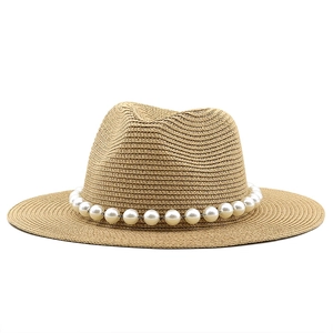 Detail of light brown straw hat featuring a wide flat brim and white faux pearl decorative band