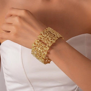 Gros plan d'un large bracelet doré avec des motifs floraux ajourés portés par un modèle