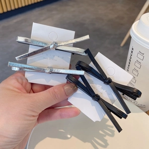 Set of four minimalist leather and silver bow hair clips on display cards in a cafe setting