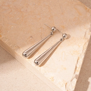 Detailed macro shot of sleek silver drop earrings resting on a textured stone base