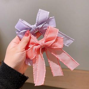 Handheld view of lavender and coral pink ribbon bow hair clips with beaded scalloped edges