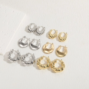 Flat lay of 14K gold and silver crescent earrings with twisted textures on a white stone background