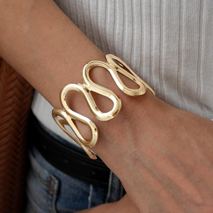 Close-up of golden wavy cuff bracelet with hollow S-shaped polished metal design