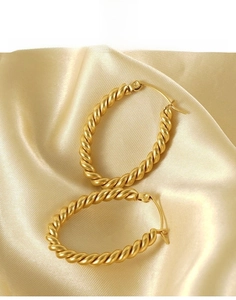 Detail of gold twisted hoop earrings made of durable titanium steel on silk fabric
