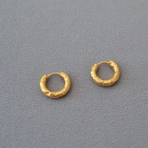 Detail shot of vintage gold hammered texture hoop earrings on a grey fabric background