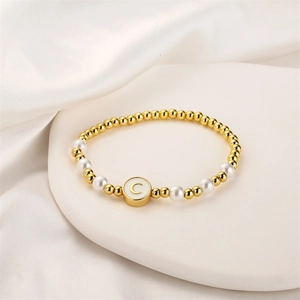 Détail d'un bracelet de perles dorées et nacrées avec pendentif lettre C en émail blanc