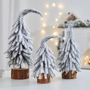 Three mini snow-flocked PE Christmas trees with natural wooden bases in a cozy setting