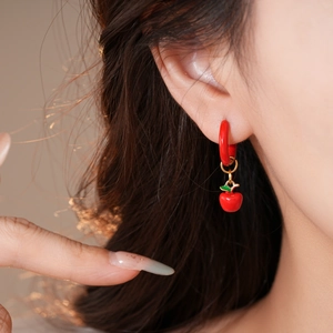 Close-up of red oil-drop apple pendant earring worn by a model in gold finish