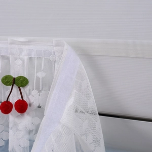 Close-up of white floral lace curtain with red cherry accents and velcro mounting tape