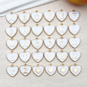 Detailed arrangement of 30 white enamel heart pendants with gold A-Z letters on beige texture