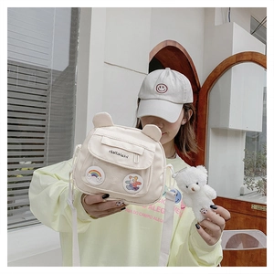 Detail of off-white canvas crossbody bag with cute animal ears and a plush bear pendant