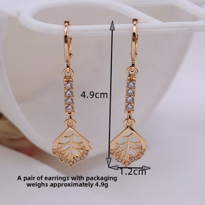 Detail shot of long gold earrings with leaf charms and zircons measuring 4.9cm by 1.2cm