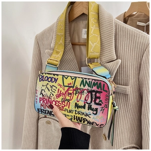 Detail of colorful graffiti crossbody bag with bold lettering and wide yellow shoulder strap