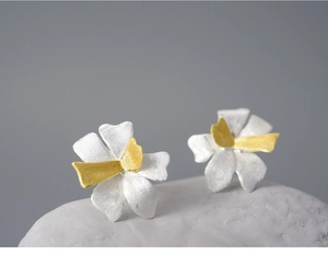 Macro shot of bicolour silver and gold flower stud earrings on white stone background